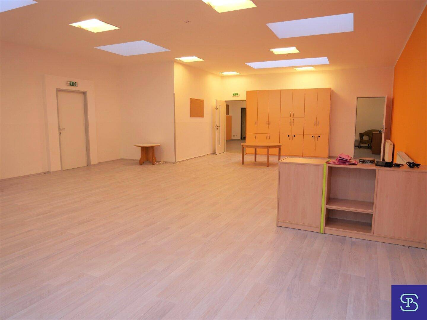 Heller Mehrzweckraum mit integrierten Holzschränken, einer orangefarbenen Akzentwand und moderner Deckenbeleuchtung.