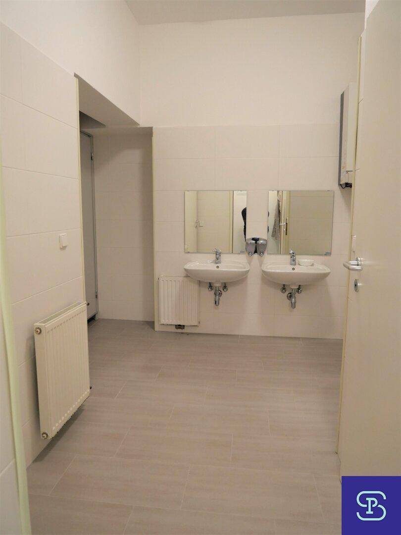 Helles, modernes Badezimmer mit zwei wandmontierten Waschbecken, großen Spiegeln und weißen Fliesen an Wänden und Boden.