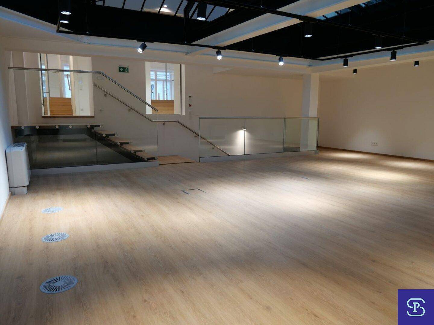 Geräumiger Wohnbereich mit Laminatboden, moderner Treppe und Glasgeländer.