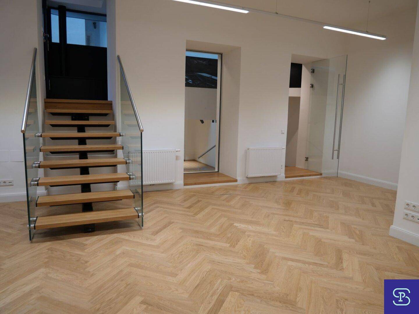Eingangsbereich mit Fischgrätparkett, moderner Holztreppe und Glasgeländer.