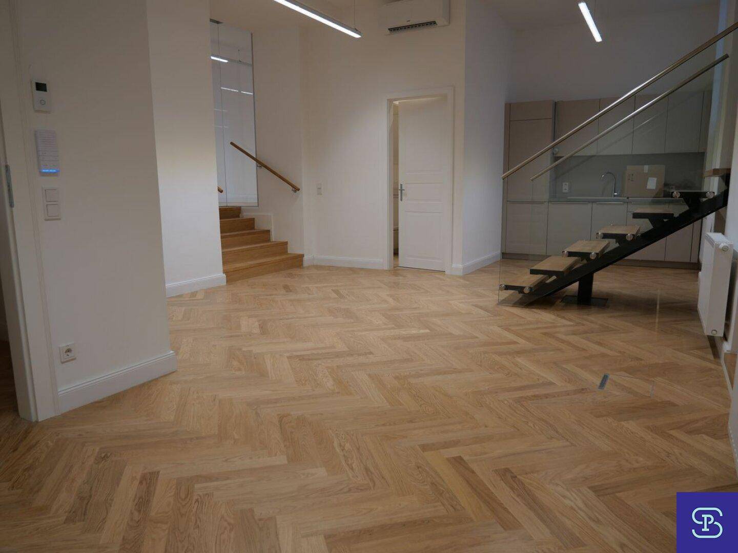 Offener Wohnbereich mit Fischgrätparkett, Treppe und integrierter Küchenzeile im Hintergrund.
