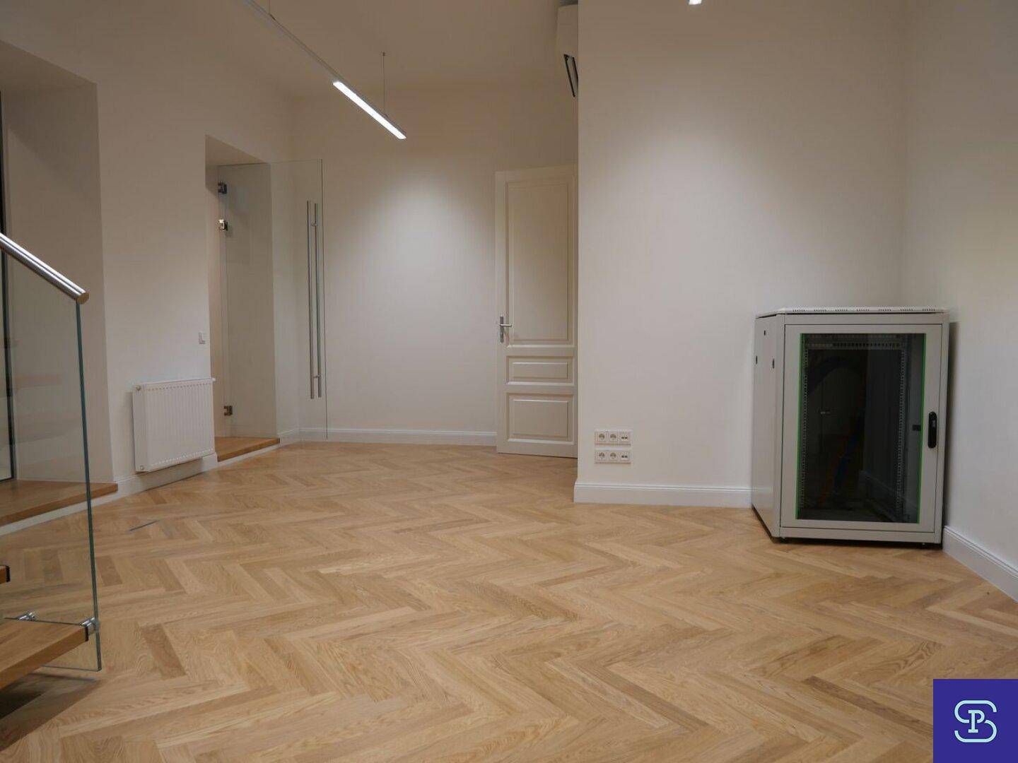 Heller Raum mit Fischgrätparkett, Tür und einem Serverschrank.