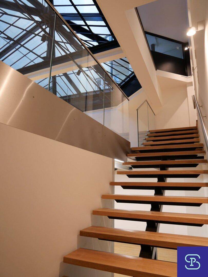 Moderne Holztreppe mit Glasgeländer und Edelstahlakzenten unter einem Glasdach.