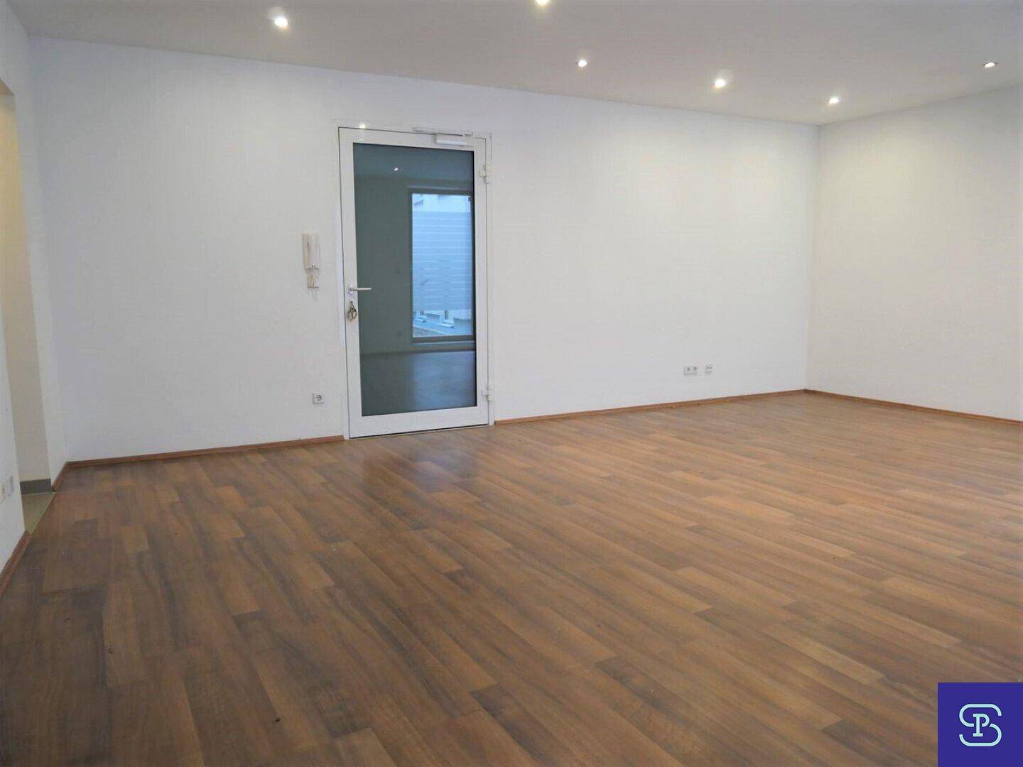 Leerer Raum mit Laminatboden, weißen Wänden und einer modernen Glastür.