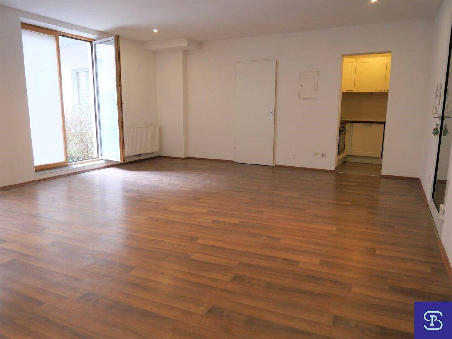 Heller Wohnbereich mit Laminatboden, Zugang zum Außenbereich und einer integrierten Küchenzeile.