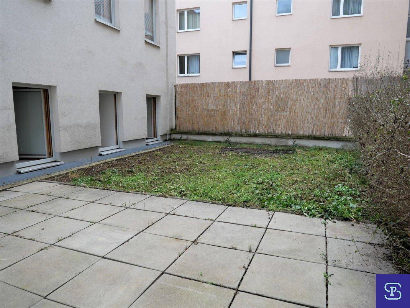 Kleiner, pflegeleichter Gartenbereich mit gepflasterter Terrasse und Bambuszaun.