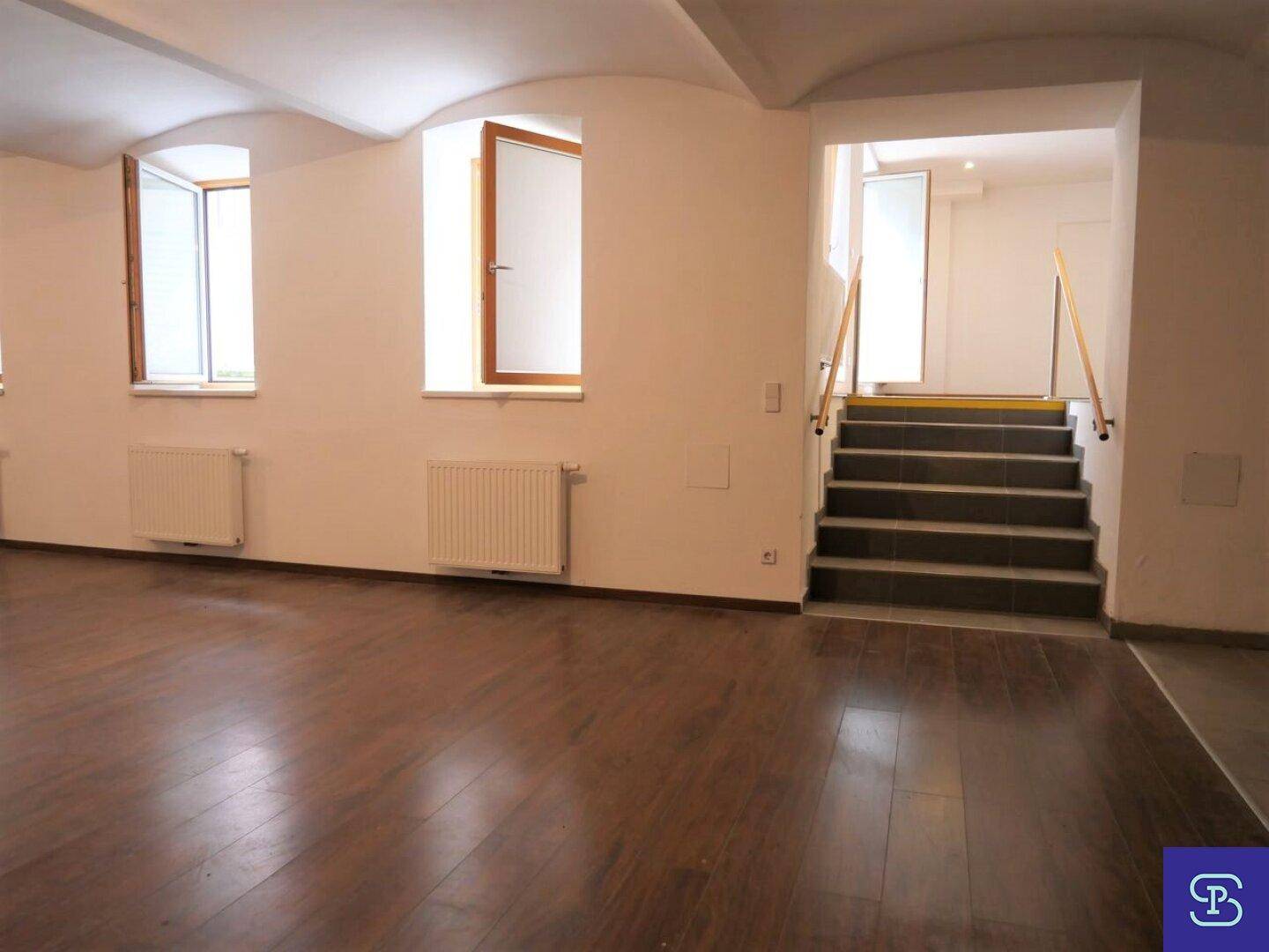Großer Raum mit Holzboden, gewölbter Decke und Fenstern, die Tageslicht hereinlassen.