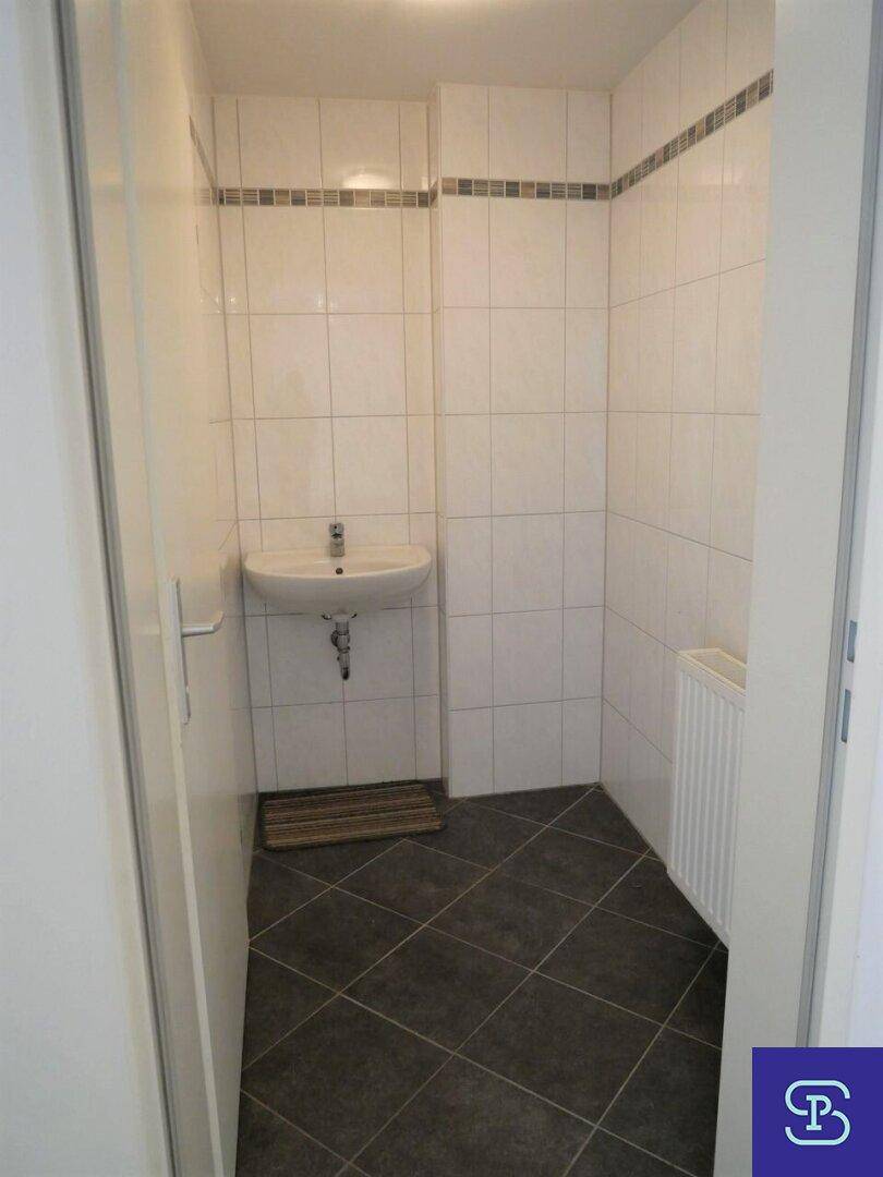 Kleines Badezimmer mit Waschbecken, weißen Fliesen und dunklem Fliesenboden.