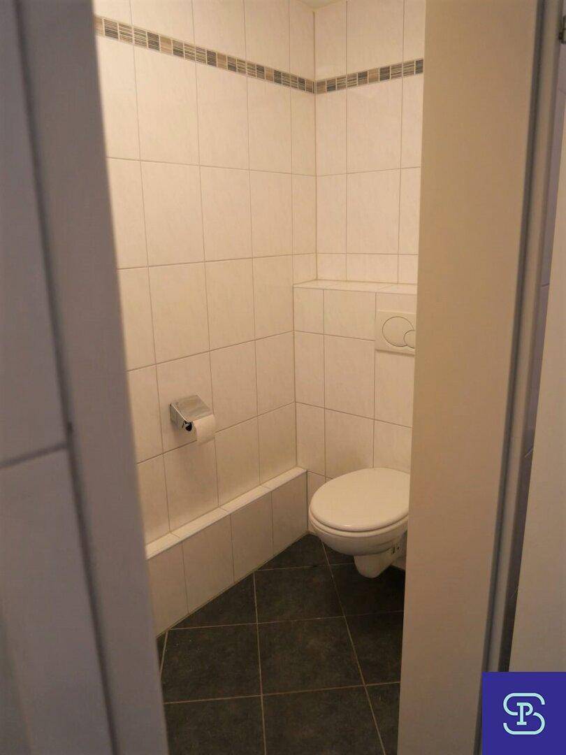 Modernes Gäste-WC mit wandmontierter Toilette, weißen Fliesen und dunklem Boden.