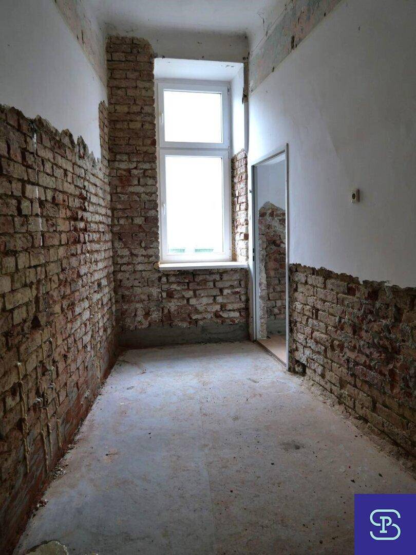 Schmaler Raum im Rohbau mit freigelegten Ziegelwänden und einem Fenster, ideal für Umbau.