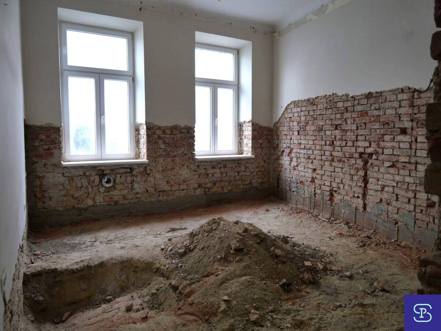 Kleinerer Raum im Rohbau mit freigelegten Ziegelwänden und zwei Fenstern, bereit zur Sanierung.