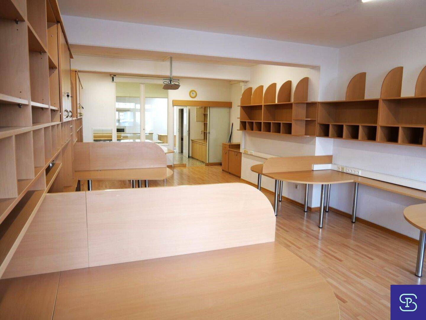 Weitläufiger Bürobereich mit zahlreichen Holzregalen und Arbeitsplätzen, durch eine Glastür verbunden.