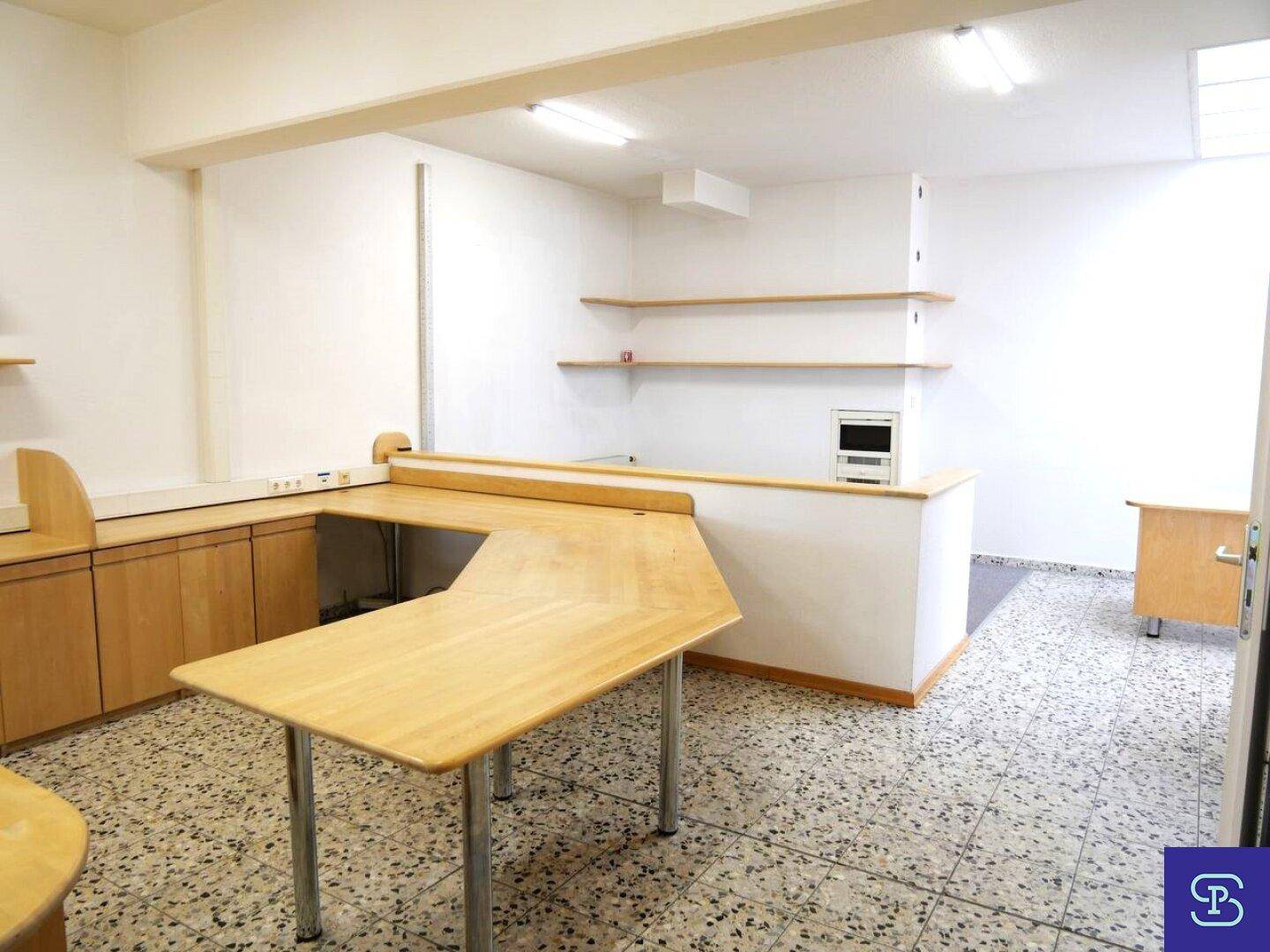 Empfangsbereich oder Arbeitsplatz mit Theke, Holzmöbeln und gefliestem Boden in Terrazzo-Optik.