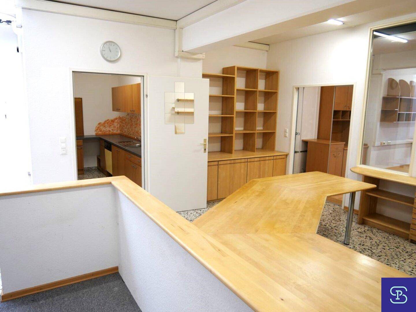 Bürobereich mit Empfangstheke, Regalen und Zugang zu einer separaten Küche.