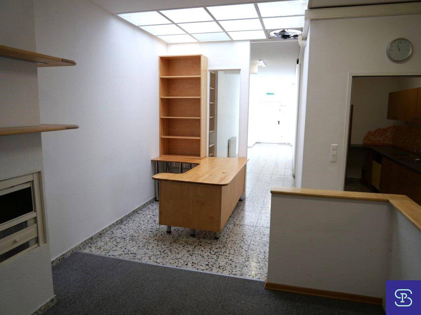 Flur oder Arbeitsbereich mit Regalen, Schreibtisch und Deckenfenstern für natürliches Licht.