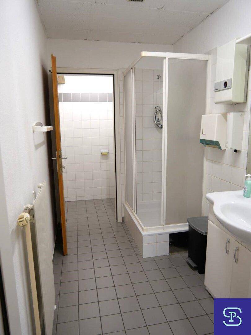 Einfaches Badezimmer mit Duschkabine, Waschbecken und weißen Fliesen an Wänden und Boden.