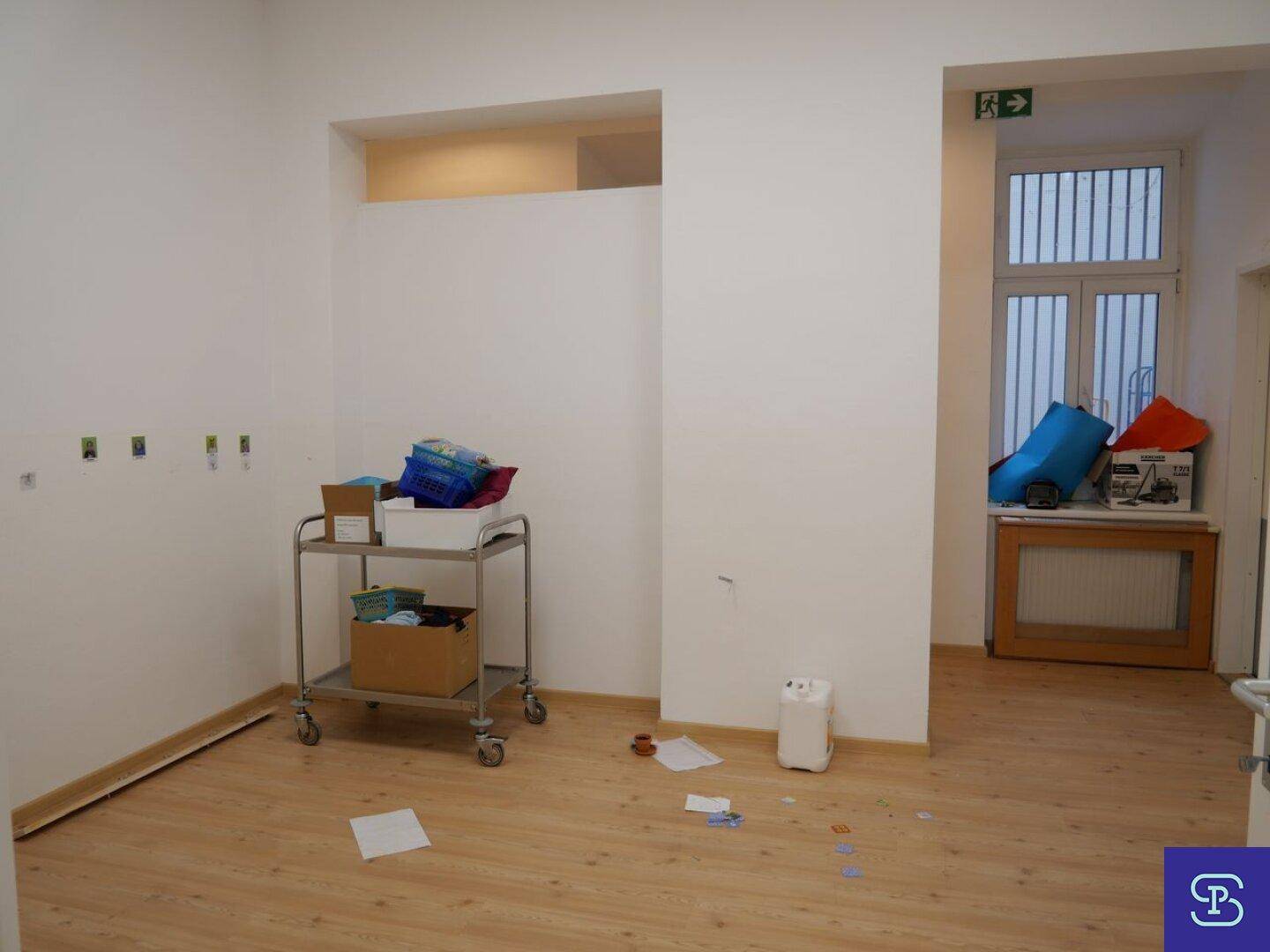 Heller Flur mit Laminatboden, weißen Wänden und einem Fenster mit Gitterstäben im Hintergrund, gut beleuchtet.