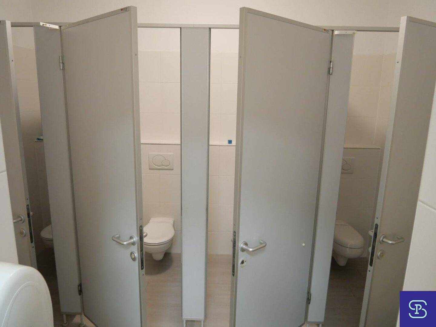 Reihe von Toilettenkabinen in einem hell gefliesten Waschraum mit modernen Wand-WCs.