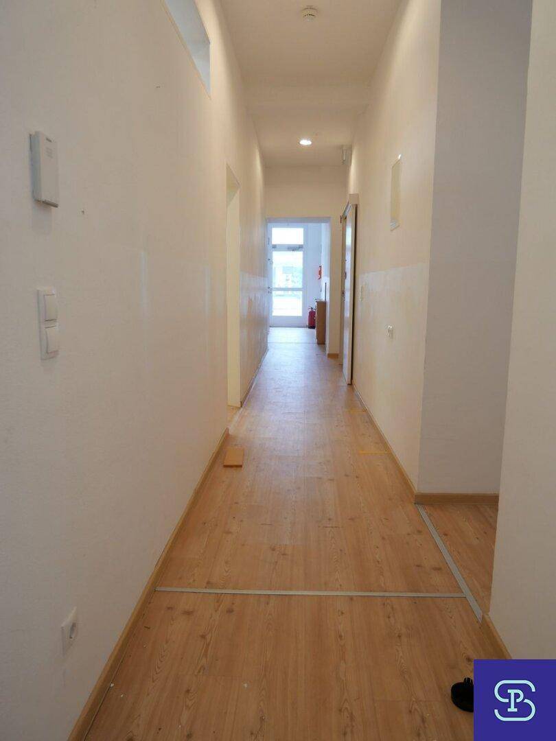 Langer, schmaler Flur mit hellem Laminatboden und weißen Wänden, der in die Ferne führt.