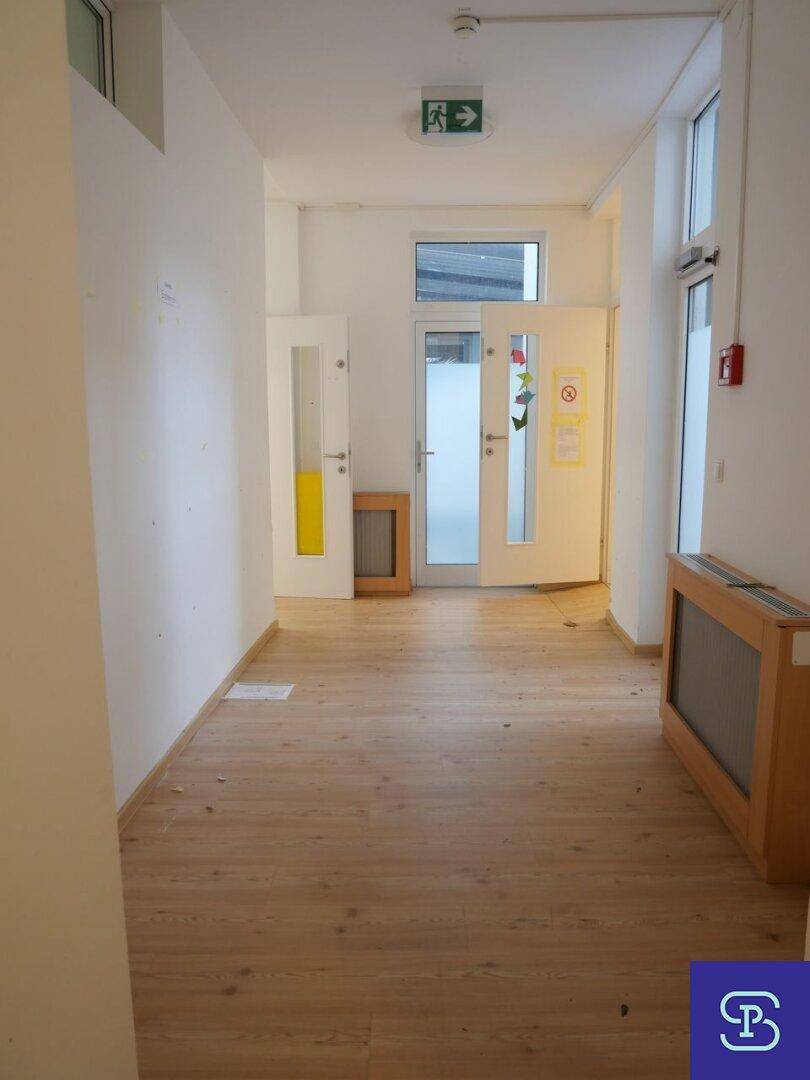 Heller Flur mit Laminatboden, weißen Wänden und einer Tür mit Glasausschnitt am Ende.