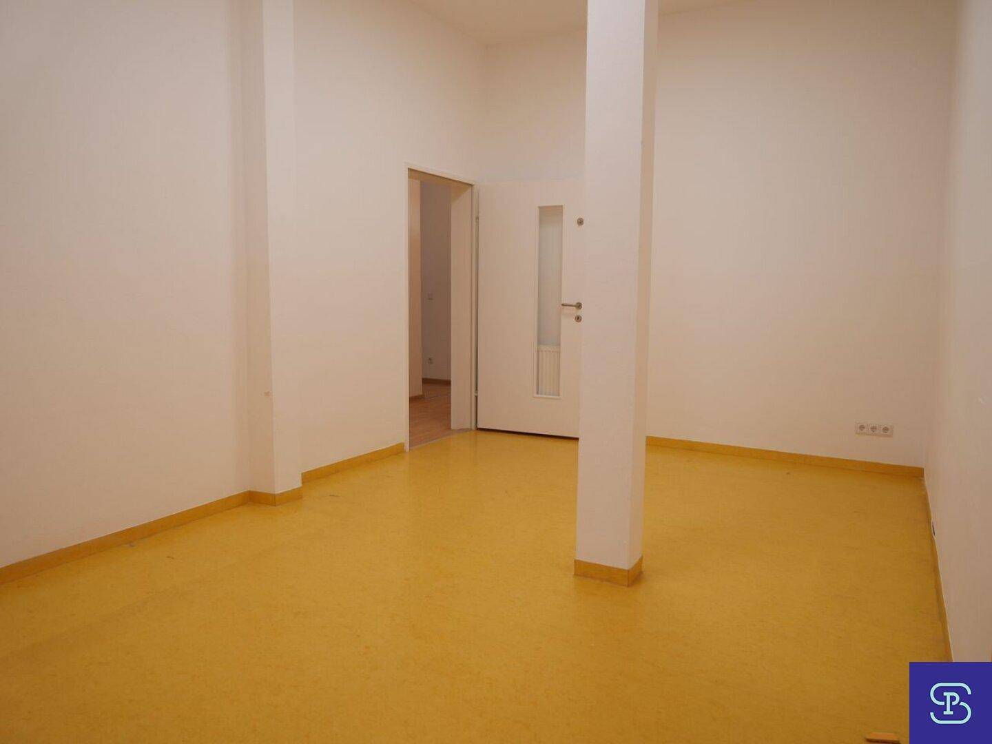 Heller Raum mit gelbem Linoleumboden, weißen Wänden und einer Tür mit Glasausschnitt, in gutem Zustand.