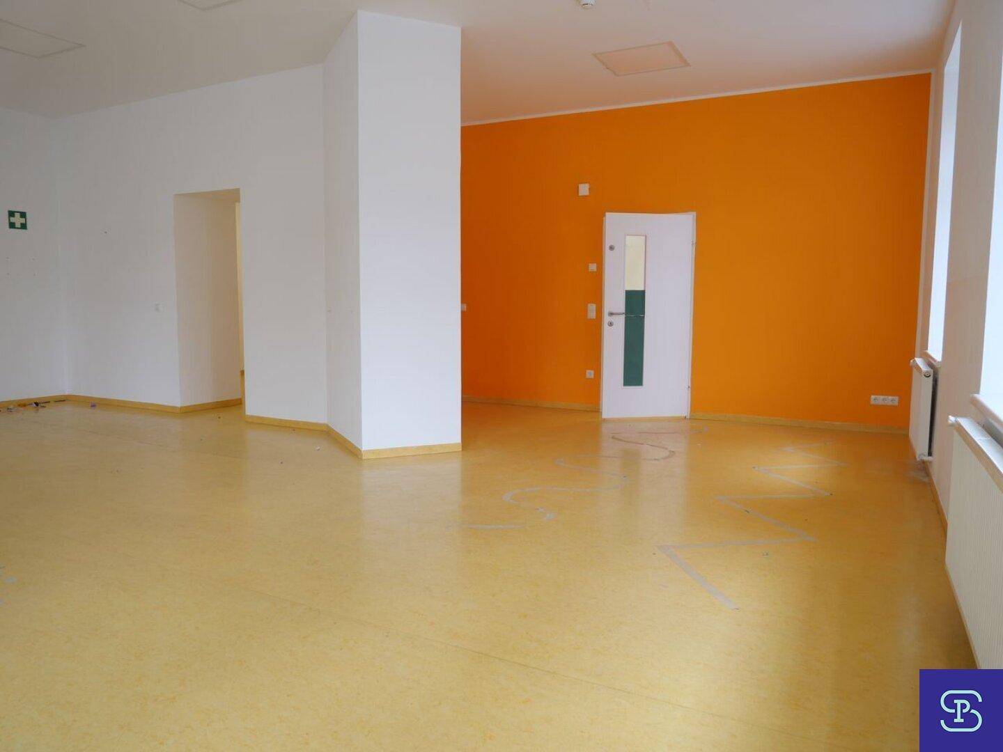 Heller Raum mit gelbem Linoleumboden, einer orangefarbenen Akzentwand und einer weißen Tür.