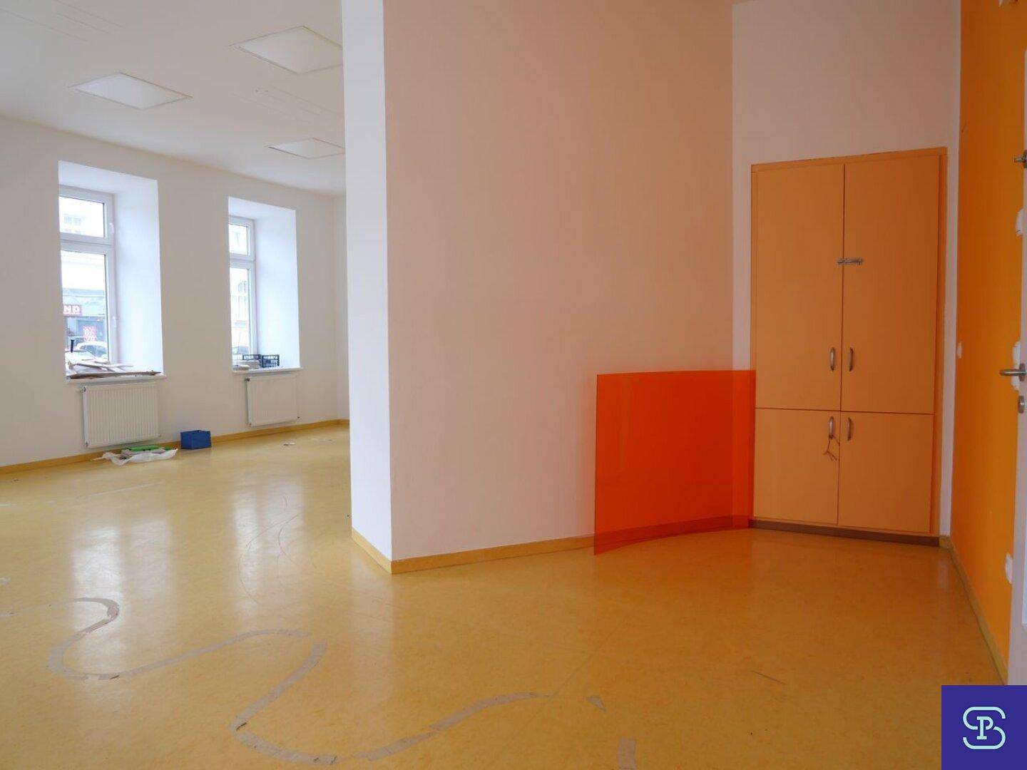 Geräumiger Raum mit gelbem Linoleumboden, orangefarbenen Schränken und einer orangefarbenen Akzentwand.