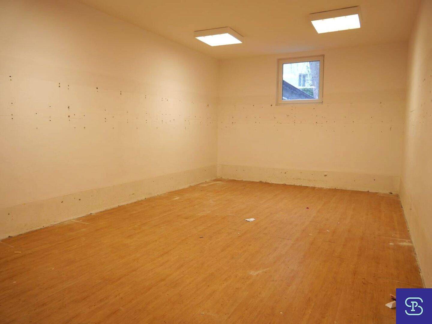 Leerer Raum mit hellem Laminatboden, beigen Wänden und einem kleinen Fenster, in gutem Zustand.