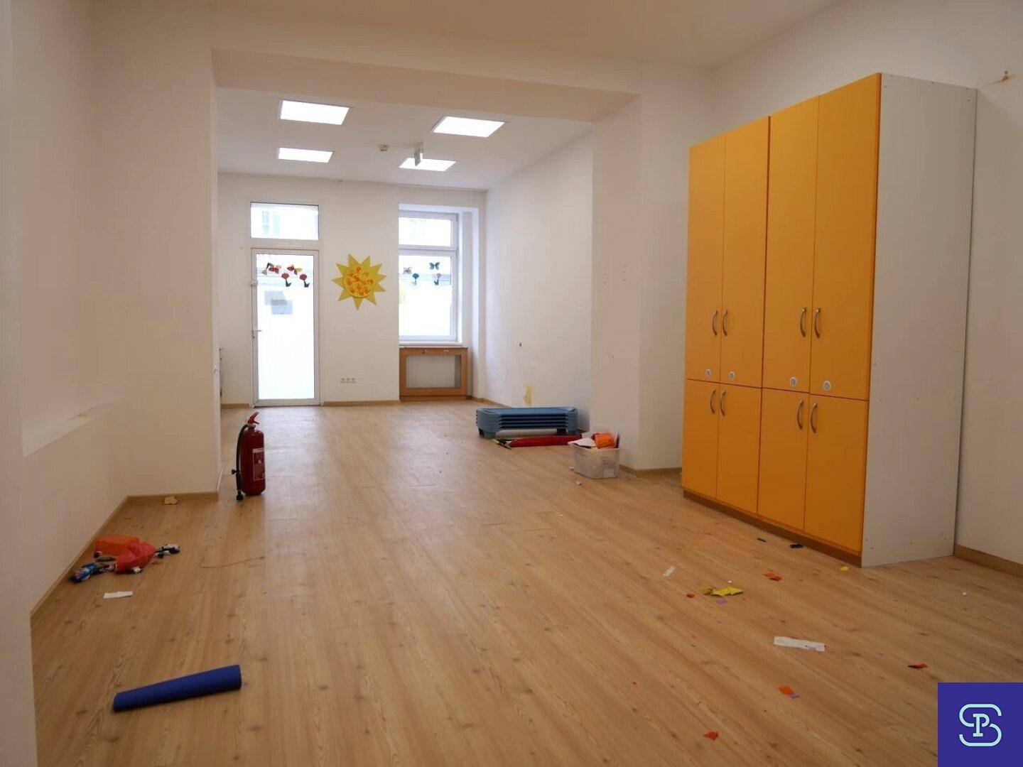 Großer, heller Raum mit Laminatboden, weißen Wänden und orangefarbenen Schränken, gut beleuchtet.