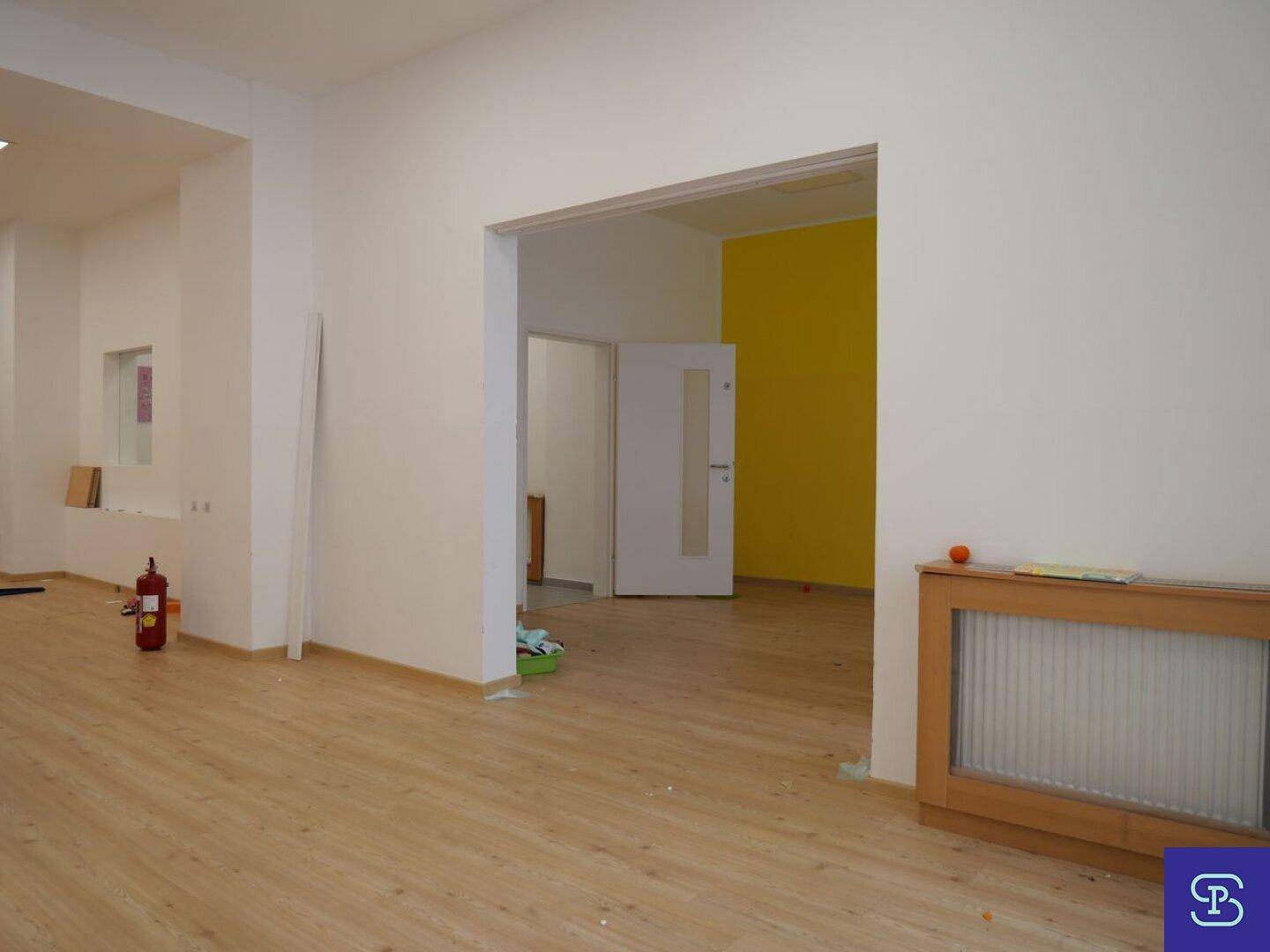 Geräumiger Raum mit Laminatboden, weißen Wänden und einem Durchgang zu einem gelben Raum.