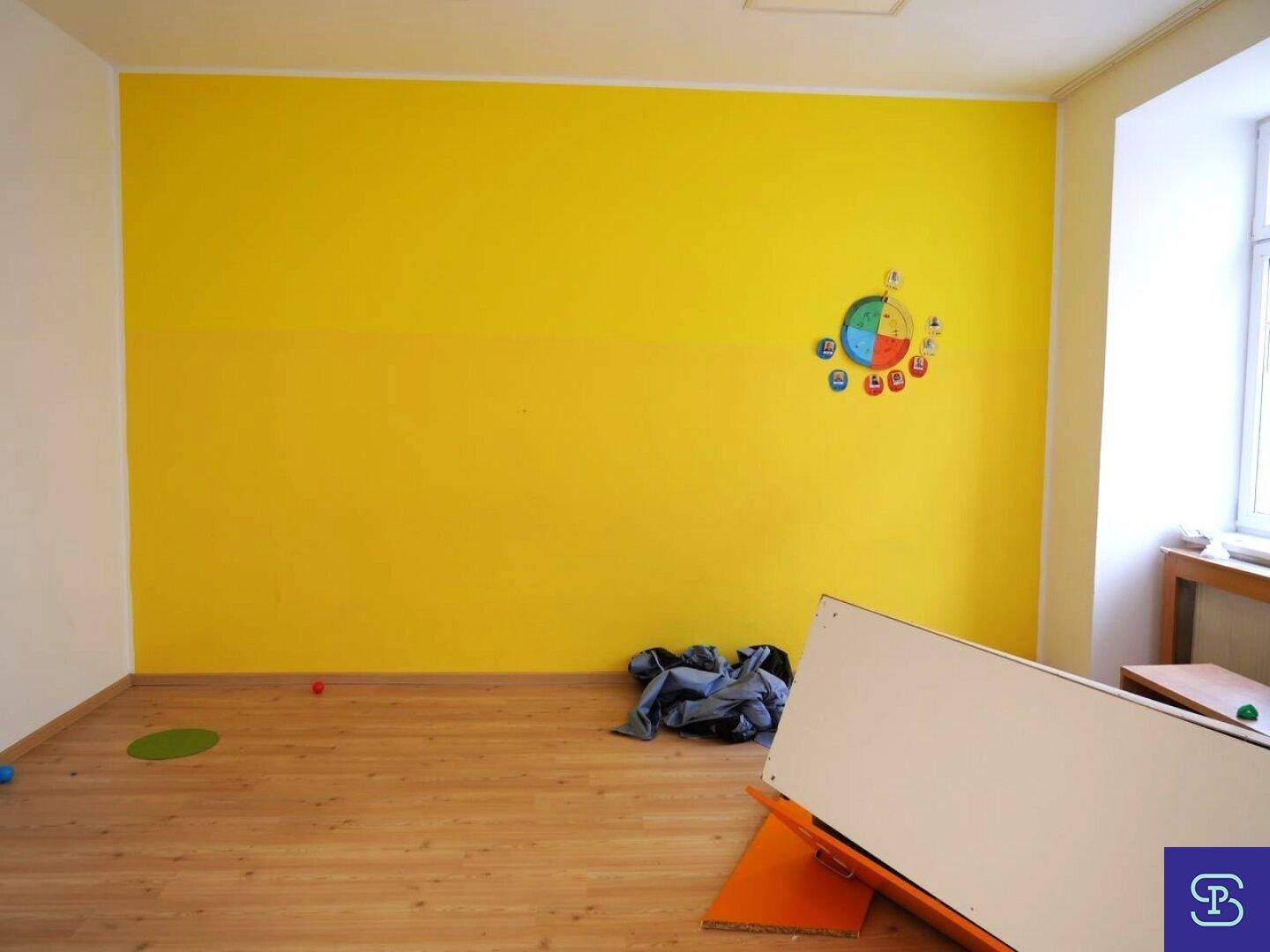 Heller Raum mit Laminatboden, einer gelben Akzentwand und einem Fenster mit Dekoration.