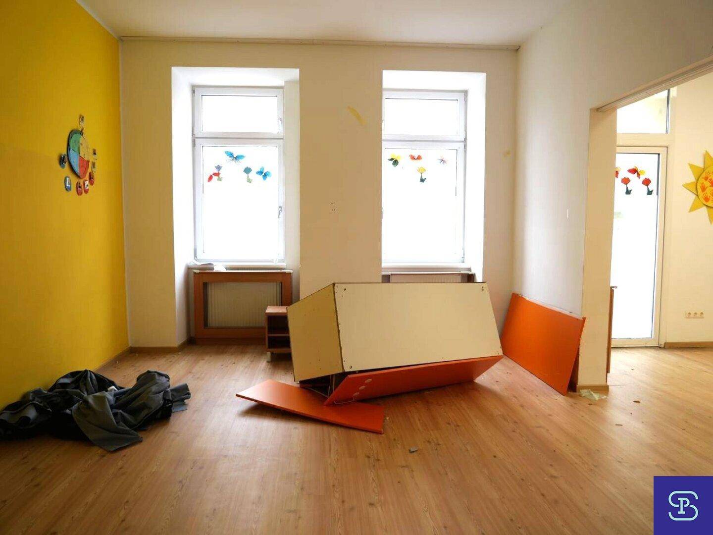 Geräumiger Raum mit Laminatboden, einer gelben Akzentwand und zwei großen Fenstern, gut beleuchtet.