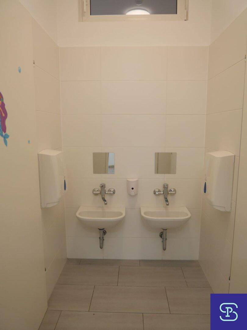 Heller Waschraum mit zwei kleinen Waschbecken, Spiegeln und weißen Wandfliesen, modern gestaltet.