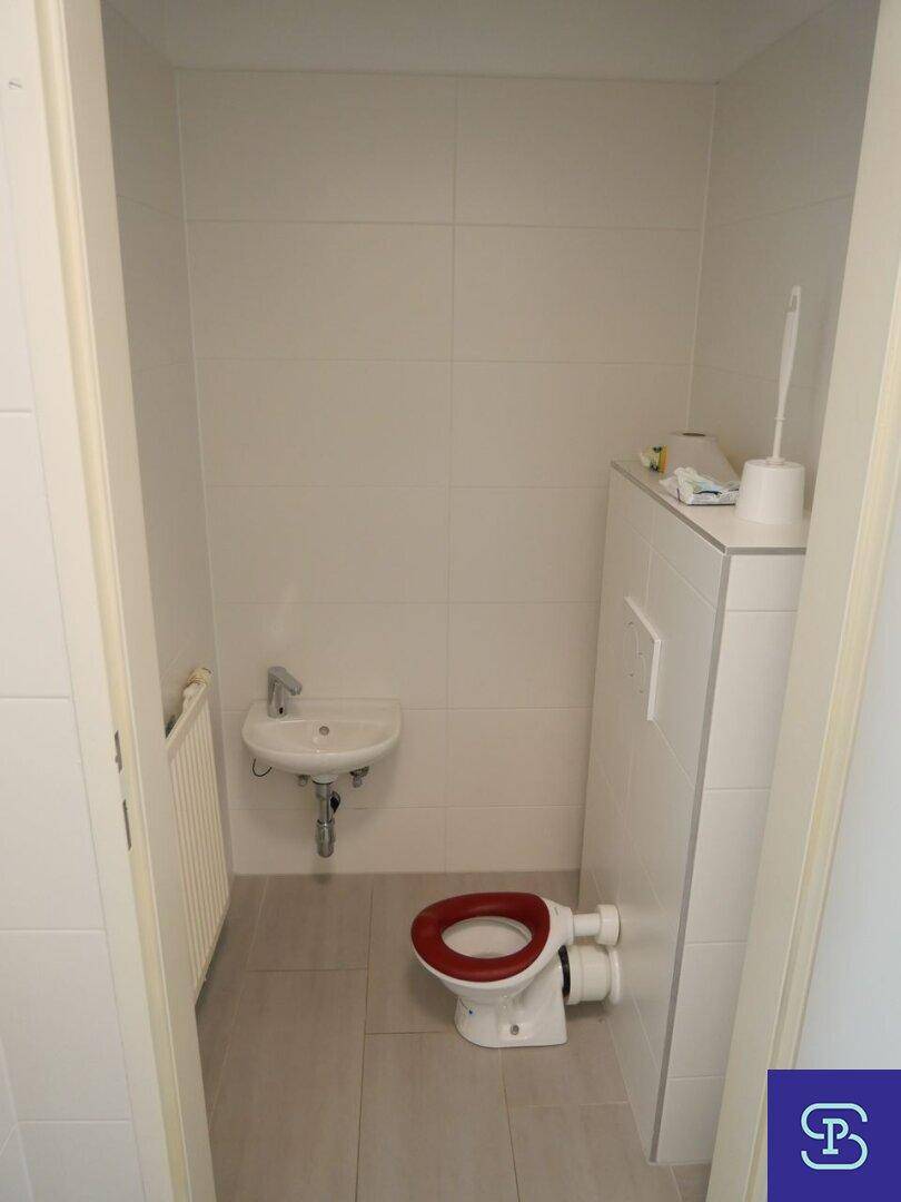 Kleine Toilettenkabine mit weißer Wandverkleidung, hellgrauen Fliesen und einem Kinder-WC.