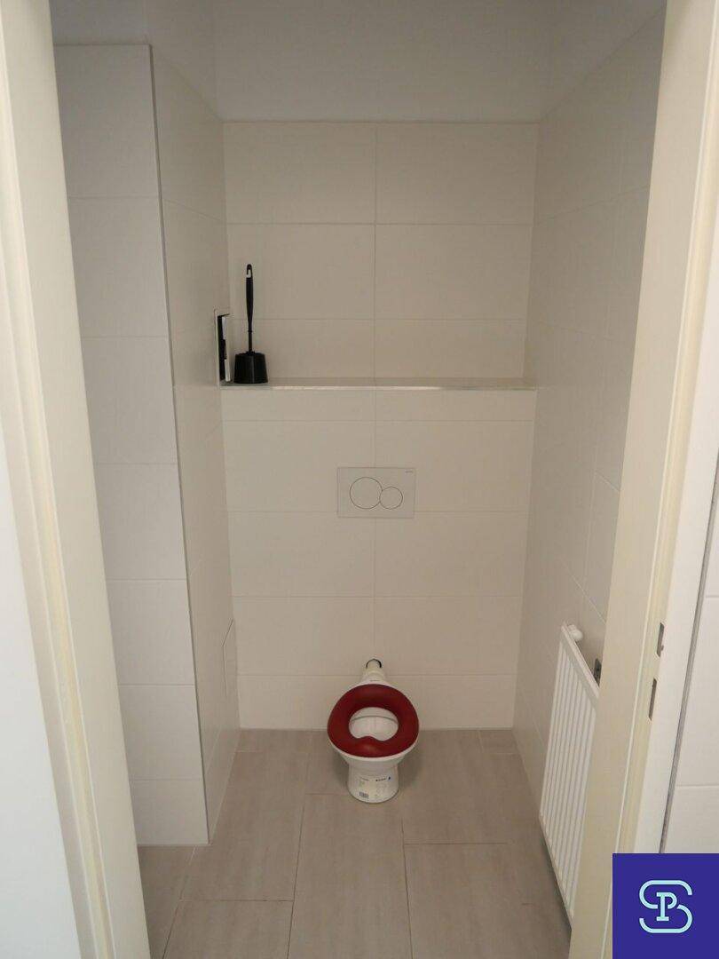 Helle Toilettenkabine mit weißer Wandverkleidung, hellgrauen Fliesen und einem Kinder-WC.