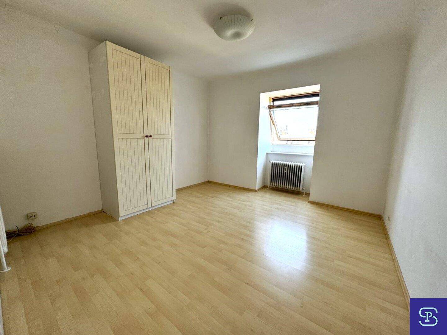 Geräumiges Schlafzimmer mit hellem Laminatboden, weißem Kleiderschrank und Dachfenster.