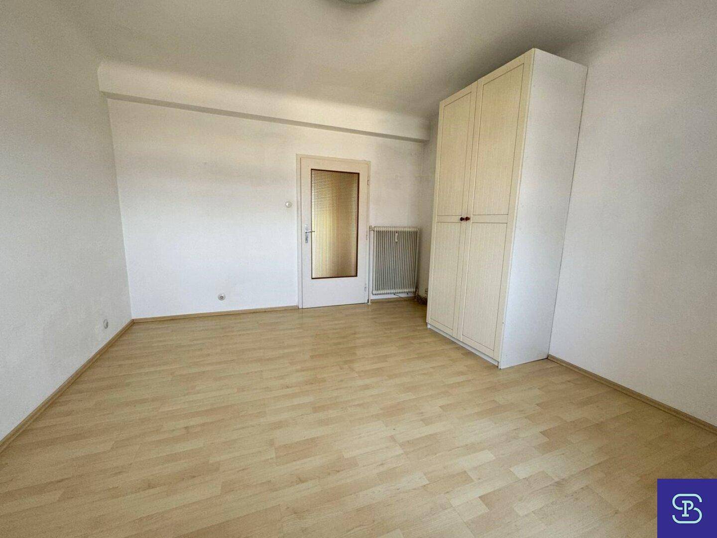 Helles Zimmer mit Laminatboden, weißem Kleiderschrank und einer Tür mit Milchglas.