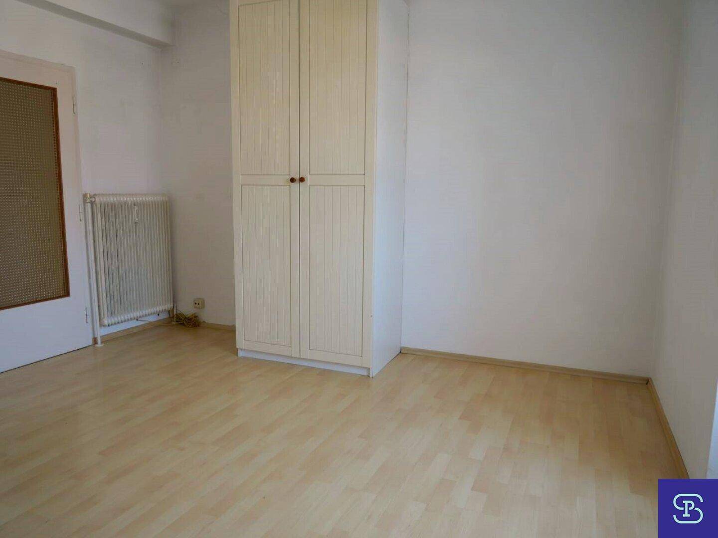 Detailansicht eines weißen Kleiderschranks in einem hellen Zimmer mit Laminatboden.