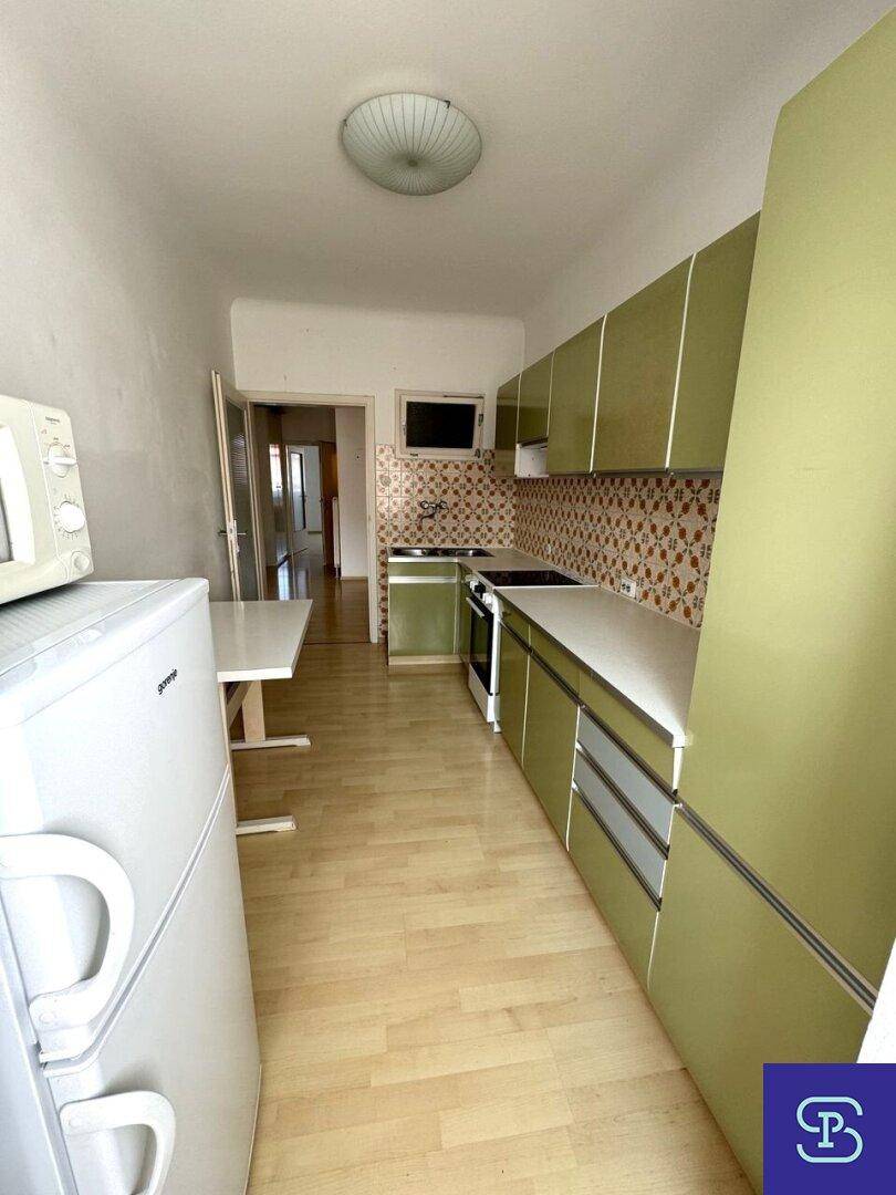 Funktionale Küche mit grünen Schränken, Kühlschrank und Mikrowelle, mit Blick zum Flur.