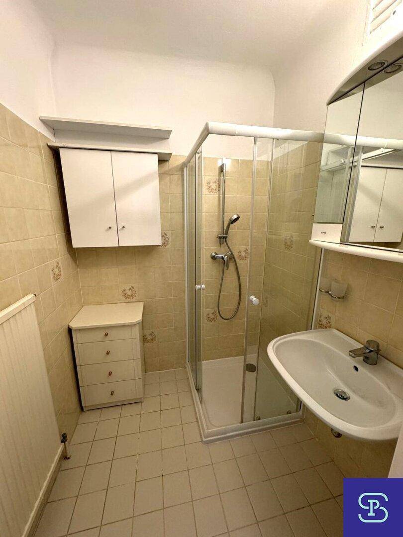 Badezimmer mit beigefarbenen Fliesen, Duschkabine, Einzelwaschbecken und Spiegelschrank.
