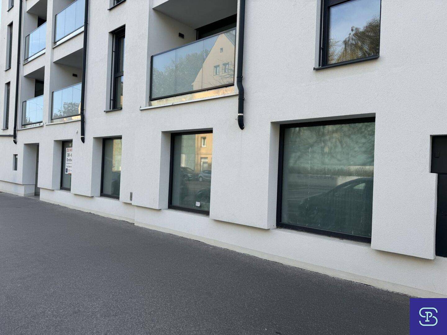 Moderne Gebäudefassade mit großen Fenstern und Balkonen mit Glasgeländern, die ein zeitgemäßes Design aufweisen.