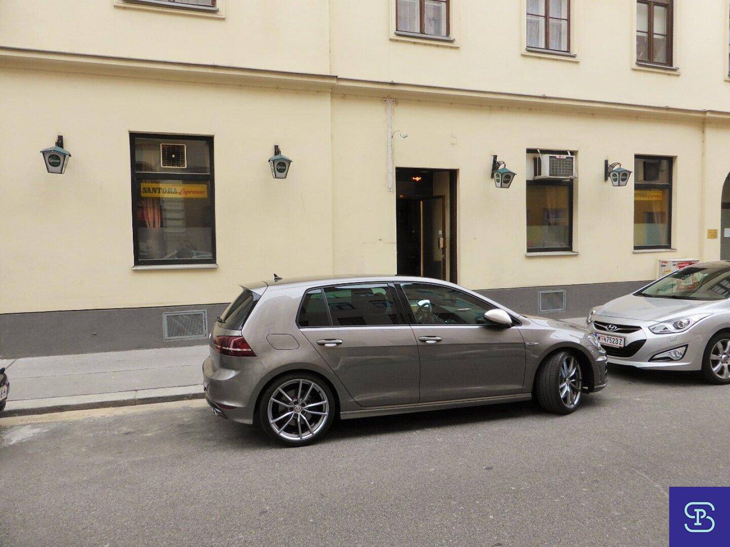 Straßenansicht eines Gebäudes mit geparkten Autos und Fenstern im Erdgeschoss.