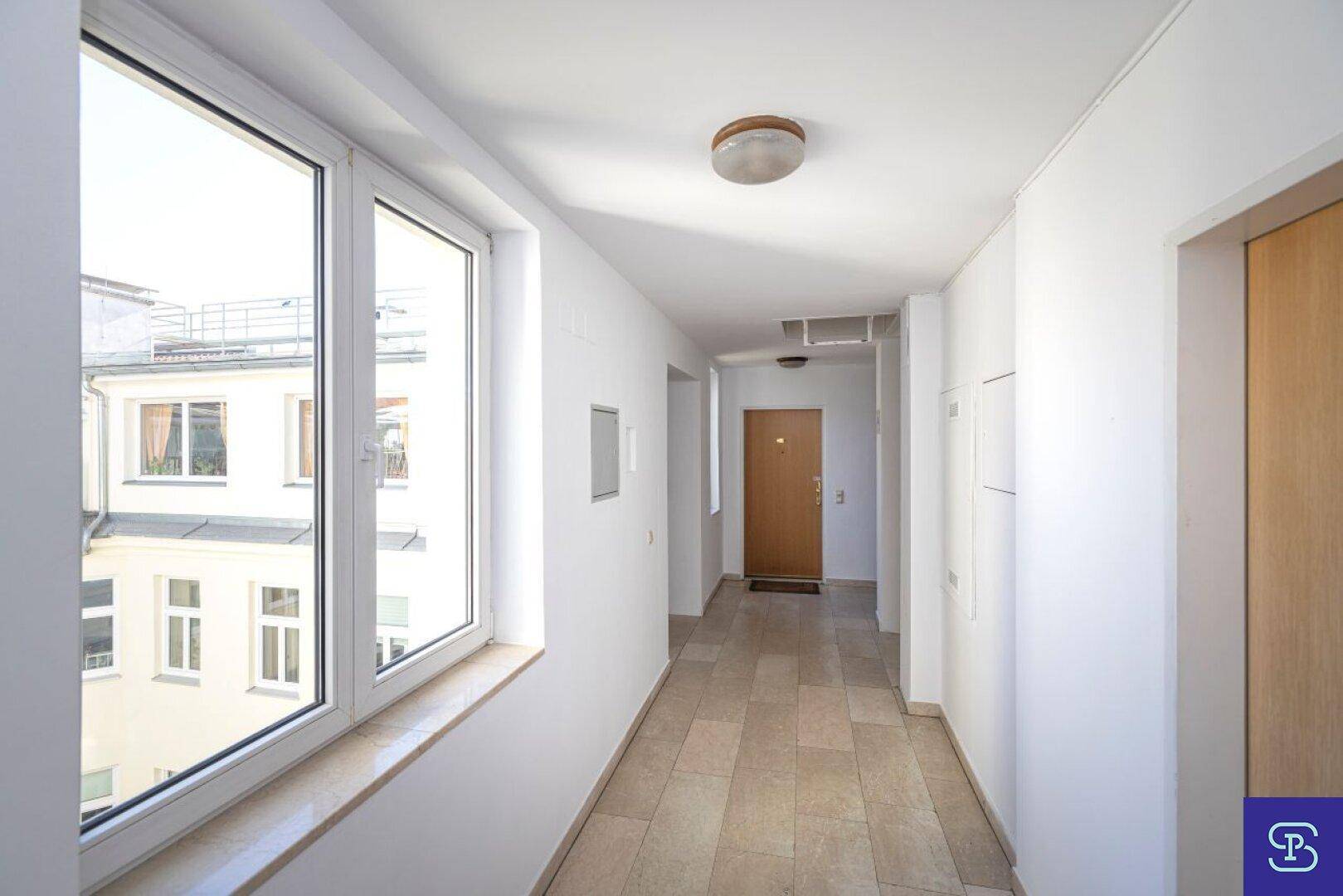 Heller und moderner Flur mit großen Fenstern, Fliesenboden und Blick auf die umliegenden Gebäude.