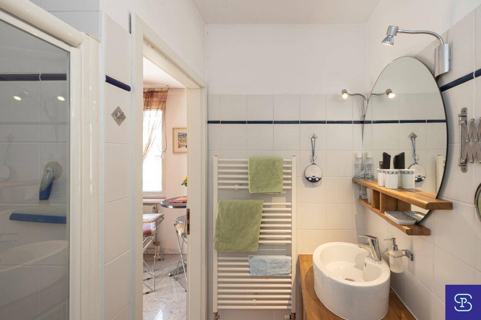 Badezimmer mit Waschtisch, beheiztem Handtuchhalter und Zugang zu einem weiteren Raum.