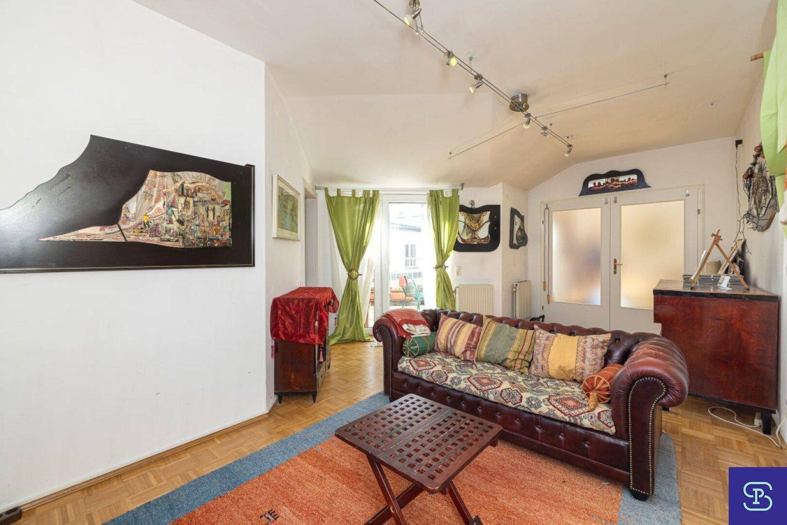 Wohnzimmer mit Ledersofa, Parkettboden und Zugang zu einem weiteren Raum.