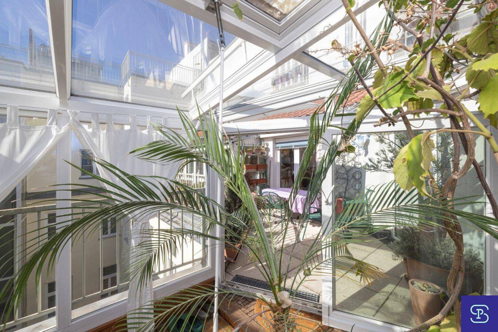 Blick durch den verglasten Wintergarten mit üppigen Pflanzen und viel Tageslicht.