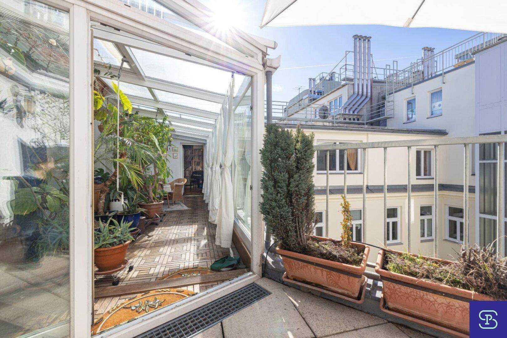 Terrasse mit Blick auf den Wintergarten und die umliegenden Gebäude, ideal für sonnige Tage.
