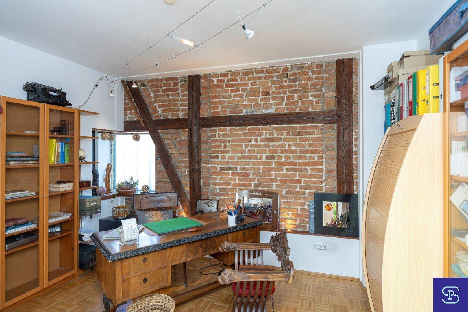 Arbeitszimmer mit freigelegten Ziegelwänden, Holzbalken und klassischem Schreibtisch.