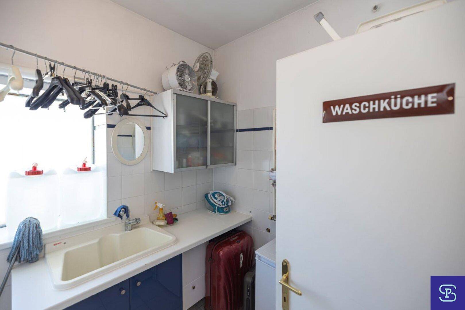Praktische Waschküche mit großem Waschbecken, Fliesenwänden und Fenster für natürliche Belüftung.