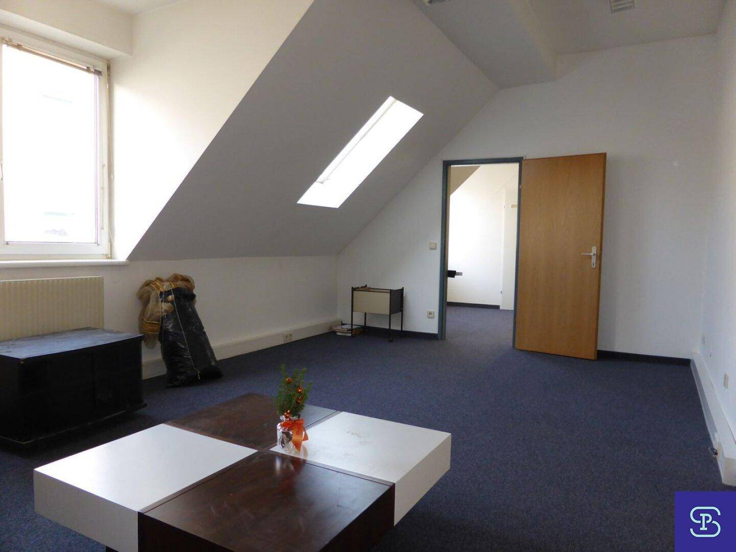 Dachgeschossraum mit Teppichboden, Dachfenster und schrägen Wänden, nutzbar als Büro oder Aufenthaltsraum.